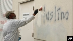 FILE - A man paints over racist graffiti on the side of a mosque in what officials were calling an apparent hate crime, in Roseville, Calif., Feb. 1, 2017.