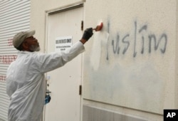 FILE - A man paints over racist graffiti on the side of a mosque in what officials are calling an apparent hate crime, in Roseville, Calif., Feb. 1, 2017.