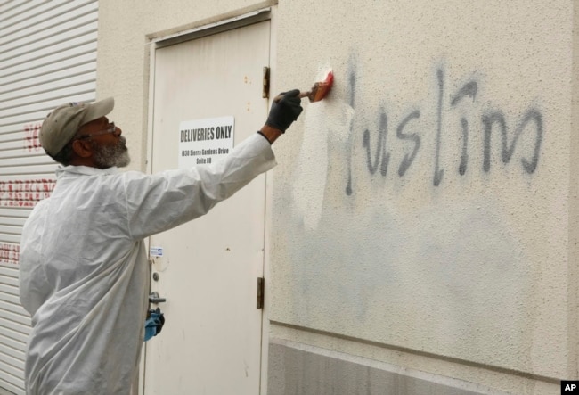 FILE - A man paints over racist graffiti on the side of a mosque in what officials are calling an apparent hate crime, in Roseville, Calif., Feb. 1, 2017.