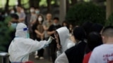 FILE - A health worker gets a swab sample from a woman to be tested for COVID-19 at a swab collection site in Beijing, May 27, 2022.