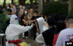 FILE - A health worker gets a swab sample from a woman to be tested for COVID-19 at a swab collection site in Beijing, May 27, 2022.