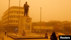 A woman walks past a statue of Iraqi poet Abdel Ghani Maarouf al Rusafi during a sandstorm in Baghdad, Iraq, May 16, 2022.