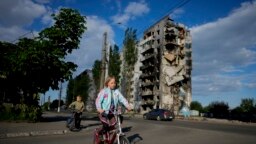 Дівчина їде на велосипеді перед зруйнованими внаслідок обстрілу будинками в Бородянці, Україна, вівторок, 24 травня 2022 р. (AP Photo/Натача Писаренко)