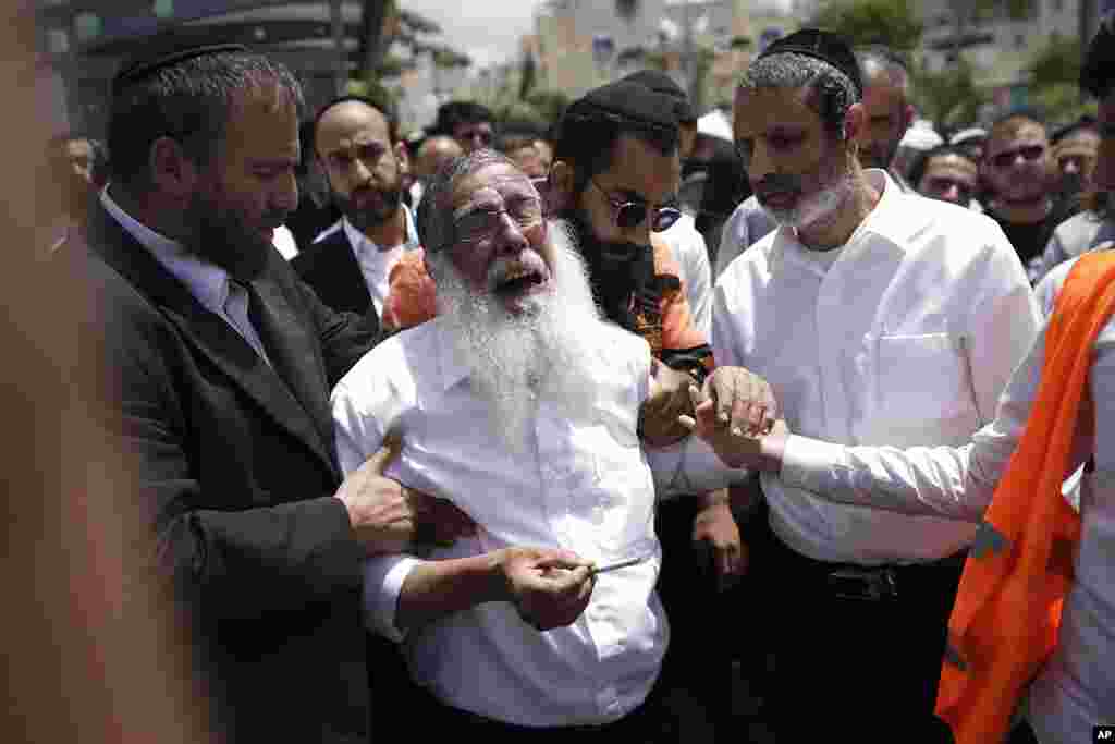 Ultra-Orthodox Jewish mourners encircle a man overcome with grief at the funeral for Yonatan Havakuk and Boaz Gol, a day after they were killed in a stabbing attack in Elad, Israel.
