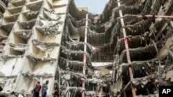 In this photo provided by Tasnim News Agency, debris hangs from the Metropol building, a 10-story commercial building under construction, in the southwestern city of Abadan, Iran, May 24, 2022.