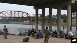 Los migrantes que cruzaron el río Bravo hacia EEUU están bajo la custodia de miembros de la Guardia Nacional mientras esperan la llegada de los agentes de la Patrulla Fronteriza en Eagle Pass, Texas, el 20 de mayo de 2022.