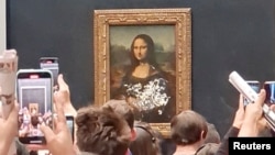 Los visitantes toman fotos y graban un video de la imagen de la "Mona Lisa", después de que hombre usara crema de pastel sobre el vidrio protector el Museo Lourve en París, Francia, el 29 de mayo de 2022 en esta captura de pantalla obtenida de un video de las redes sociales.