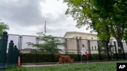 A pedestrian and their dog walk past fencing that blocks off the area around the U.S. Supreme Court Sunday, May 8, 2022, in Washington.