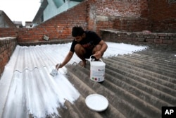 A person paints his rooftop with cool white reflective paint which brings down indoor temperature in summer, in Ahmedabad, India, May 23, 2022. (AP Photo/Ajit Solanki)