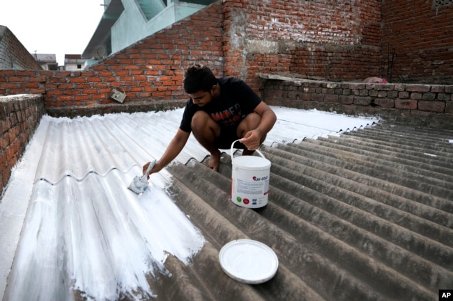 A person paints his rooftop with cool white reflective paint which brings down indoor temperature in summer, in Ahmedabad, India, May 23, 2022. (AP Photo/Ajit Solanki)