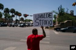 Alex Covarrubias, 32, mengacungkan plakat di sudut jalan untuk para korban penembakan di Sekolah Dasar Robb di Uvalde, Texas, 26 Mei 2022. (Foto: AP)