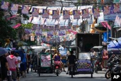 Warga melewati poster kampanye pemilu di dekat tempat pemungutan suara di Manila, Filipina. (Foto: AP)