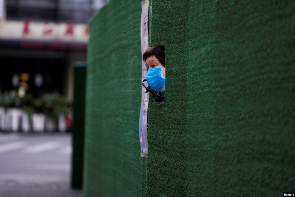 一位上海居民从封闭小区的围栏空隙中伸出头来张望。（2022年5月6日）(photo:VOA)