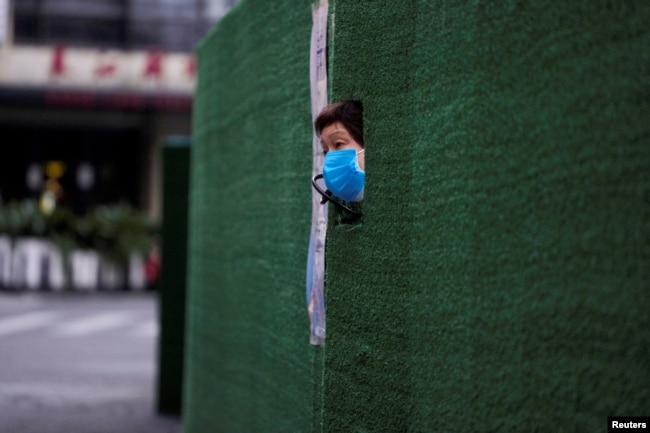 一位上海居民从封闭小区的围栏空隙中伸出头来张望。（2022年5月6日）
