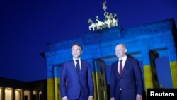 Французький президент Еммануель Макрон та німецький канцлер Олаф Шольц біля освітлених кольорами українського прапора Бранденбурзьких воріт у Берліні 9 травня 2022 р.
