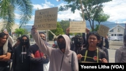 Massa aksi menyuarakan tuntutan mereka melalui tulisan di karton dalam aksi unjuk rasa di depan kantor Gubernur Sulawesi Tengah di Palu, pada 24 Mei 2022. (Foto: VOA/Yoanes Litha)