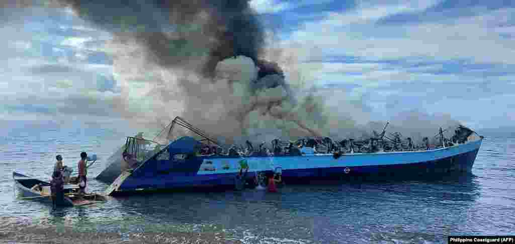 People throwing buckets of water onto a smouldering ferry which had caught fire near Real town, Quezon province, Philippines.