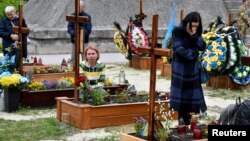 People pay respect next to graves at Lychakiv Cemetery where some people killed in Russia's invasion of Ukraine are buried as the Day of Heroes of the Heavenly Hundred is celebrated, in Lviv, Ukraine, May 22, 2022. 