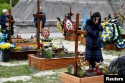 Des personnes se recueillent près de tombes au cimetière de Lychakiv à Lviv, en Ukraine, le 22 mai 2022.