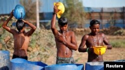 FILE - Workers use their helmets to pour water to cool themselves off near a construction site on a hot summer day on the outskirts of Ahmedabad, India, April 30, 2022. 