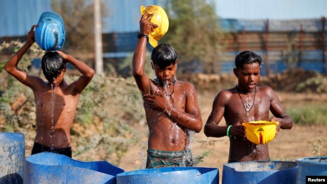 FILE - Workers use their helmets to pour water to cool themselves off near a construction site on a hot summer day on the outskirts of Ahmedabad, India, April 30, 2022.