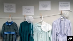 Dresses donated by sexual assault survivors from Amish and other plain-dressing religious groups hang on a clothesline beneath a description of each survivors' age and church affiliation, on April 29, 2022, in Leola, Pa. 