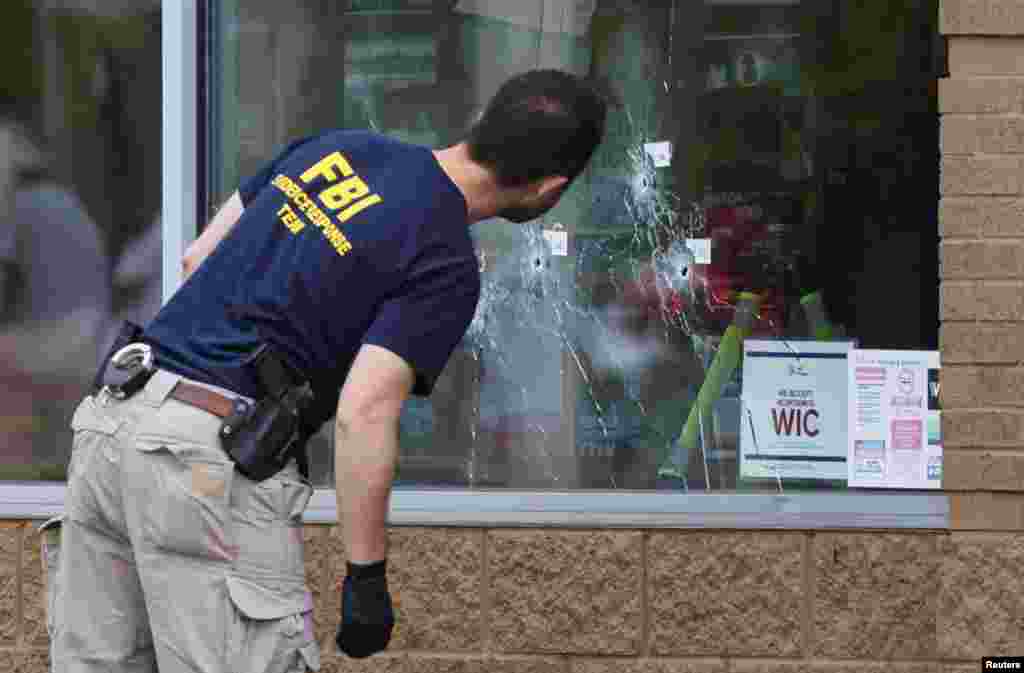 A member of the FBI looks at bullet holes through the glass at the scene of a shooting at a Tops supermarket in Buffalo, New York, May 16, 2022.