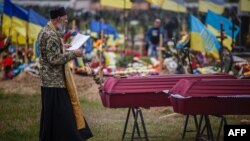 A chaplain leads a funeral service for Ukrainian servicemen Sergiy Profotilov and Igor Malenkov, both killed in the village of Vilkhivka during the Russian invasion of Ukraine, in the military section of Kharkiv cemetery number 18 in Bezlioudivka, eastern
