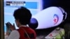 A woman walks past a television screen showing file footage of a North Korean missile test during a news broadcast in Seoul on May 12, 2022, after Seoul's military said it had detected three short-range ballistic missiles fired from near Pyongyang. 
