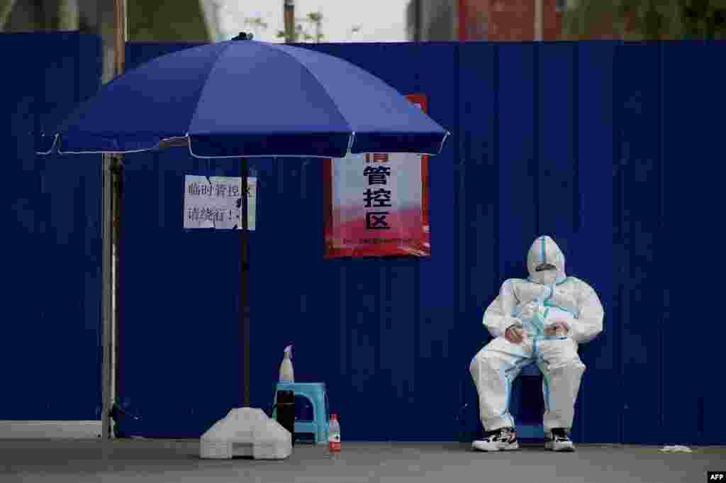 A security guard wearing personal protective equipment sleeps next to an entrance of a residential area under lockdown due to COVID-19 restrictions in Beijing.