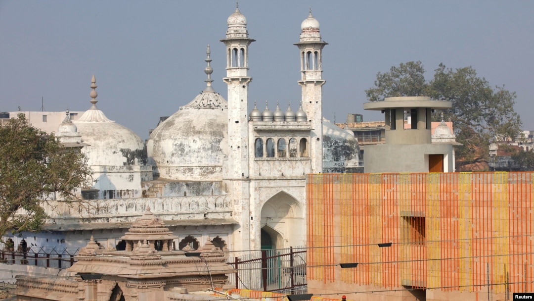 FILE -: A worker stands on a temple rooftop adjacent to the Gyanvapi Mosque in the northern city of Varanasi, India, December 12, 2021.