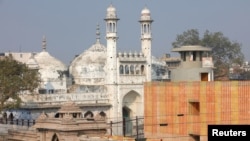 FILE -: A worker stands on a temple rooftop adjacent to the Gyanvapi Mosque in the northern city of Varanasi, India, December 12, 2021.