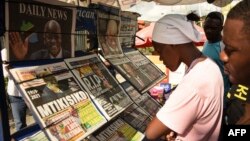 FILE - People read newspaper headlines at a news stand in Dar es Salaam, Tanzania, March 18, 2021.