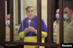 FILE - Georgian former President Mikheil Saakashvili, who was convicted in absentia of abuse of power during his presidency and arrested upon his return from exile, holds a candle in a defendant's dock during a court hearing in Tbilisi, Georgia, March 17, 2022.