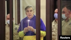 FILE - Former Georgian President Mikheil Saakashvili, who was convicted in absentia of abuse of power during his presidency and arrested upon his return from exile, holds a candle in a defendant's dock during a court hearing in Tbilisi, Georgia, March 17, 2022. 