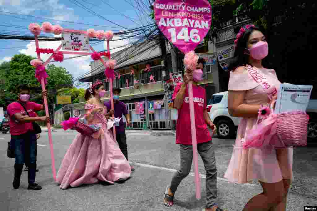 Women wearing gowns walk along a street during a Santacruzan-themed house-to-house campaign for Philippine Vice President and presidential candidate Leni Robredo, in Quezon City, Metro Manila.