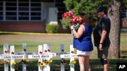 A couple prepare to place flowers on crosses with the names of children killed outside of the Robb Elementary School in Uvalde, Texas, May 26, 2022.