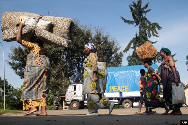 FILE - A group of Democratic Republic of Congo asylum-seekers carrying their belongings walk past a truck reading "PEACE" at the Bunagana border point in Uganda, on Nov. 10, 2021, during fighting between M23 rebels and DRC troops.