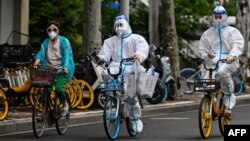 FILE - Workers wearing personal protective equipment (PPE) cycle on a street during a Covid-19 coronavirus lockdown in the Jing'an district of Shanghai, China, May 29, 2022.