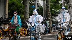 Workers wearing personal protective equipment (PPE) cycle on a street during a Covid-19 coronavirus lockdown in the Jing'an district of Shanghai, China, May 29, 2022.