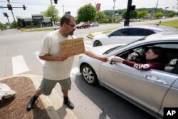 Adam Atnip, who is homeless and lives in his car, accepts money from a driver as he panhandles, May 10, 2022, in Cookeville, Tenn.