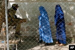 FILE - A Taliban fighter stands guard as two women enter the government passport office in Kabul, April 27, 2022. Afghanistan's Taliban leadership has ordered all Afghan women to wear the all-covering burqa in public.