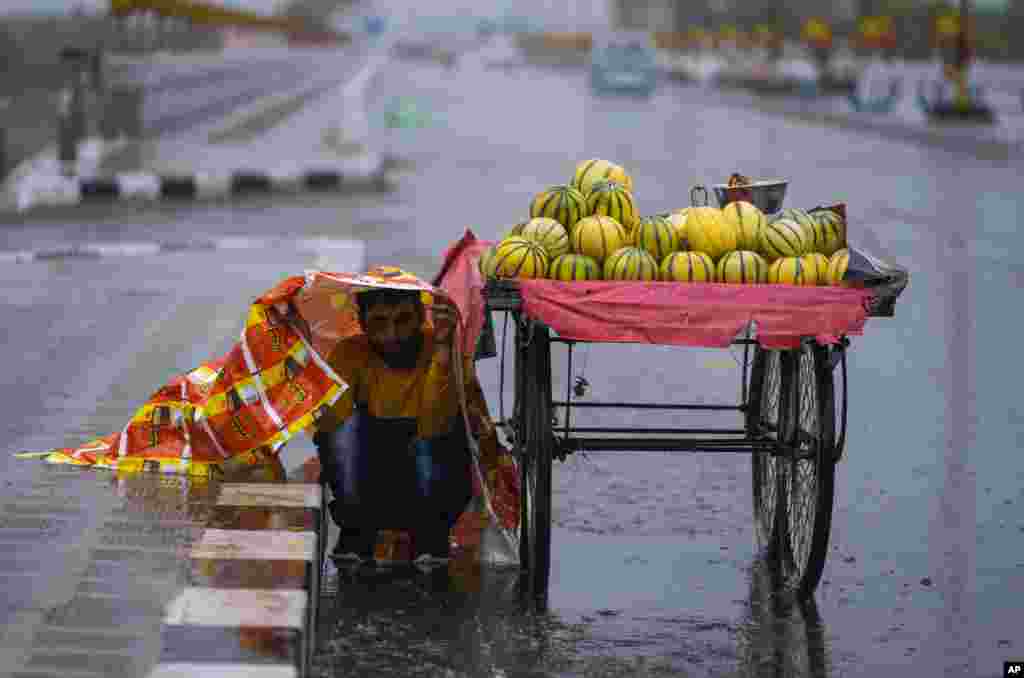 A fruit vendor covers himself with a plastic sheet as it rains in Jammu, India.