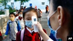 Seorang guru mengukur suhu tubuh seorang siswi untuk membantu mengekang penyebaran virus corona sebelum memasuki Sekolah Dasar Kim Song Ju di Distrik Pusat di Pyongyang, Korea Utara. (Foto: AP)