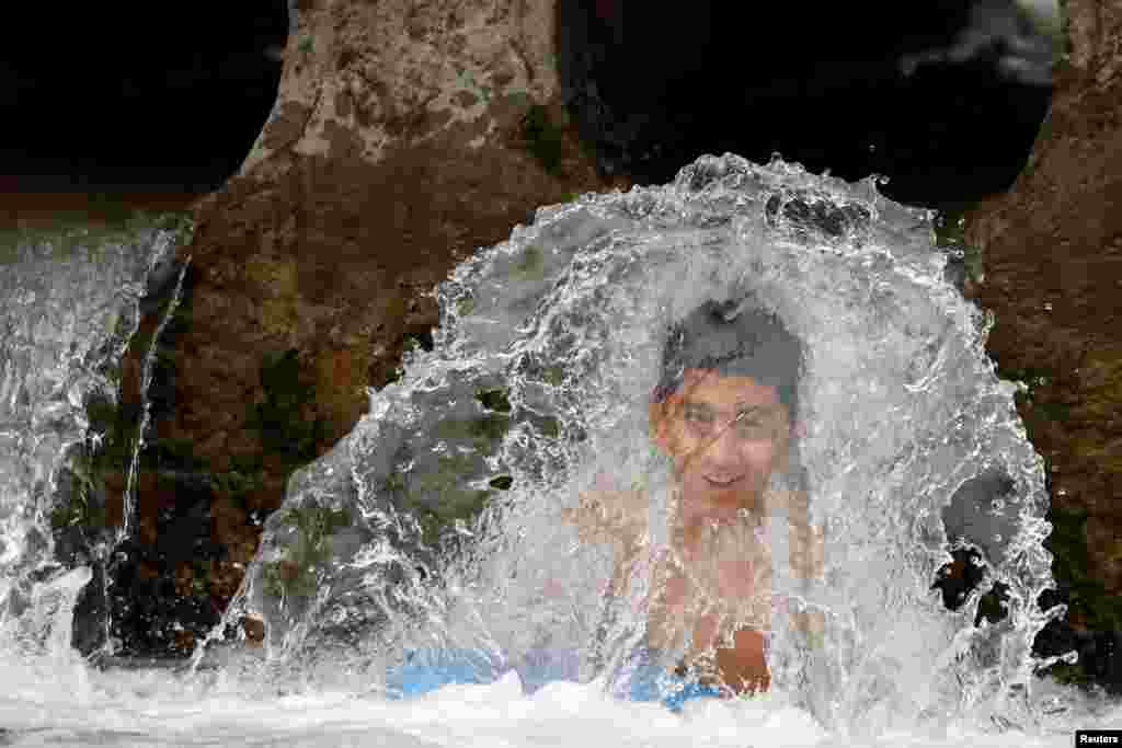 A boy bathes in a stream of water during a hot and humid day in Peshawar, Pakistan.