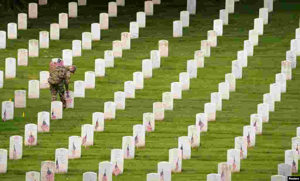 A soldier of the 3rd U.S. Infantry Regiment (The Old Guard) places flags on headstones ahead of Memorial Day at Arlington National Cemetery in Arlington, Virginia.