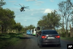 A Russian military helicopter flies over buses with Ukrainian servicemen evacuated from the besieged Mariupol's Azovstal steel plant traveling to a prison in Olyonivka, territory under the government of the Donetsk People's Republic, eastern Ukraine, May 17, 2022.