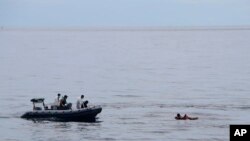 In this photo released by the National Search and Rescue Agency (BASARNAS), rescuers retrieve survivors floating on a wooden plank during a search for victims of a sinking cargo boat in the Makassar Strait, Indonesia, Sunday, May 29, 2022. (BASARNAS via AP)