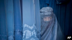 ARCHIVO - En esta fotografía de archivo del jueves 11 de abril de 2013, una mujer afgana mira a través de la abertura para los ojos de su burka mientras espera para probarse uno nuevo en una tienda en el casco antiguo de Kabul, Afganistán.