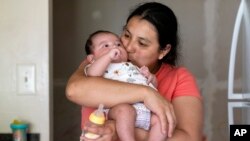 FILE - Yury Navas of Laurel, Md., kisses her two-month-old son, Jose Ismael Gálvez, after making him a bottle of formula with the only formula he can take without digestive issues, Enfamil Infant, at their apartment in Laurel, Md., May 23, 2022. 